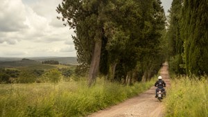 Motociclista en una Royal Enfield recorriendo una tranquila carretera rural con cipreses en la Toscana